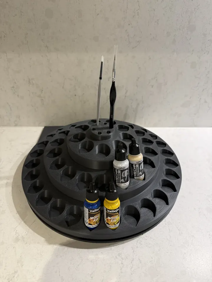 A black three-tier paint carousel holding hobby paints and brushes
